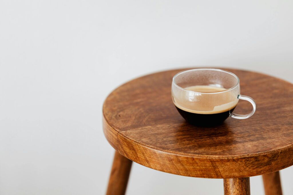 A close-up image of a fresh cup of coffee. The coffee is dark and rich, with a light layer of crema on the surface, indicating it is freshly brewed. The background is a clean, bright white, making the cup and coffee the central focus of the image.