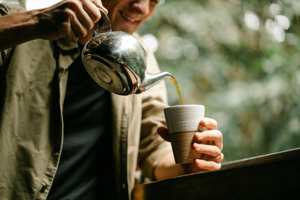 A man pouring black coffee into a cup from a silver pot.