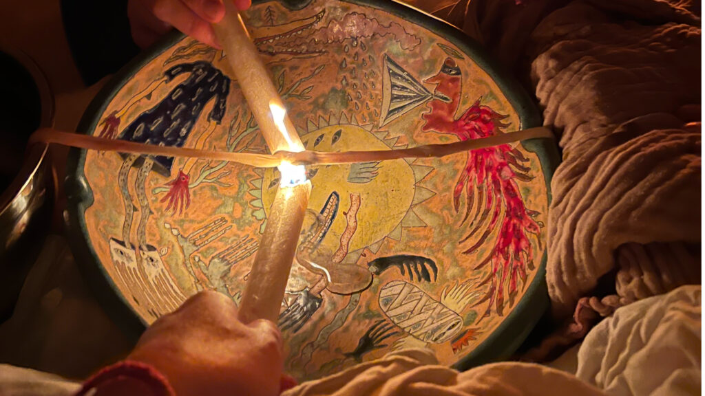 Two candles burning through an umbilical cord over a colourful bowl.