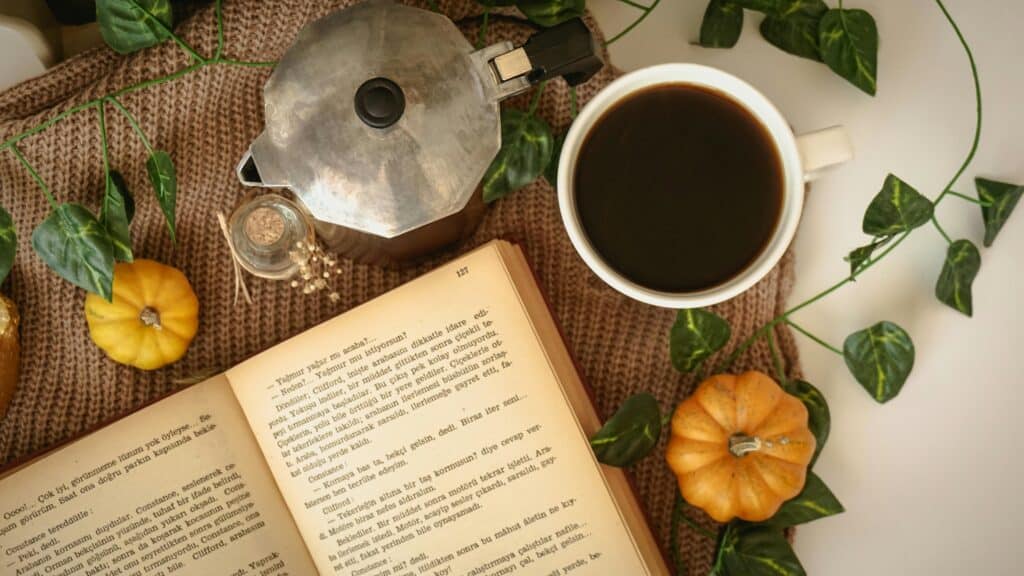 Autumn themed background with ivy leaves and little pumpkins. Moccha machine and black coffee in a white mug next to a vintage looking book.